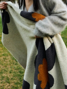 Detailed knit texture of beige sunflower blanket with soft orange and black floral patterns