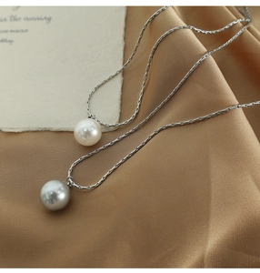 Detailed close-up of white and grey pearl pendants on silver necklaces over gold silk