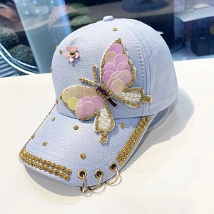 Détail de la casquette bleu clair avec papillon en paillettes et strass dorés sur le bord