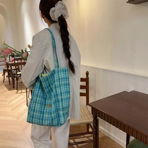 Detailed view of the large capacity blue plaid canvas tote bag used in a cozy cafe setting