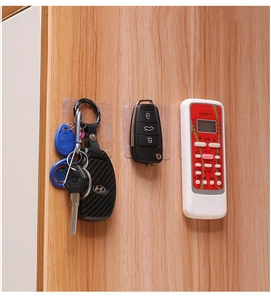 Transparent adhesive wall hooks holding keys and a remote on a wooden surface
