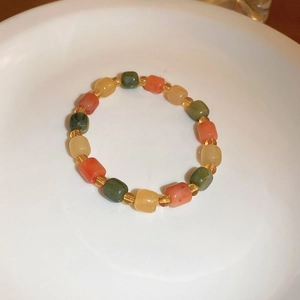 Detail showing forest green and coral orange cylindrical beaded bracelet on a white ceramic plate