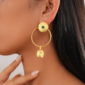 Close-up of 24K gold plated hoop earrings with spiral texture and green gemstone on model