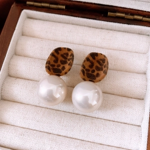Detail of flocking leopard print earrings with large faux pearls in a wooden box