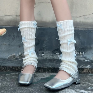 Détail de jambières en maille crème avec nœuds bleus et chaussures Mary Jane argent