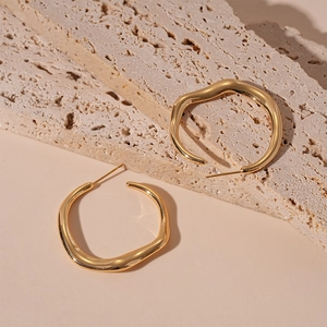Detailed close-up of golden irregular geometric hoop earrings on natural stone texture
