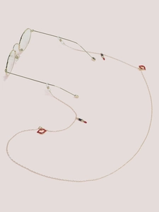 Detail of golden glasses chain with red lip and lipstick enamel charms on a pink surface
