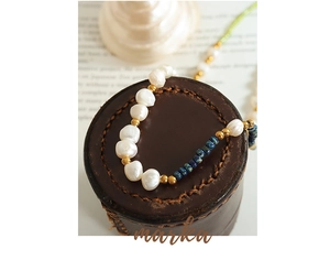Detail of freshwater pearl necklace with blue beads resting on a vintage leather case
