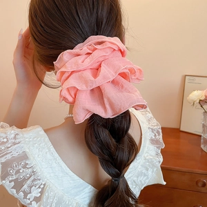 Detail of a large pink ruffled organza scrunchie styled on a braided hairstyle