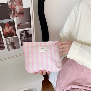 Close-up of pink striped cotton cosmetic bag with woven label held by hand
