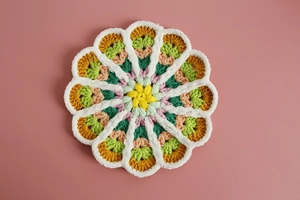 Close-up of hand-knitted flower coaster featuring colorful gradient yarn and intricate stitching