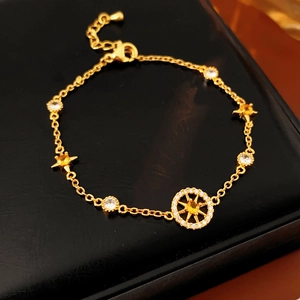 Detail of gold star and compass bracelet with zircons on a black leather background