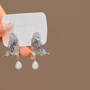 Detailed shot of silver butterfly earrings with grey-blue stones and pearl pendants
