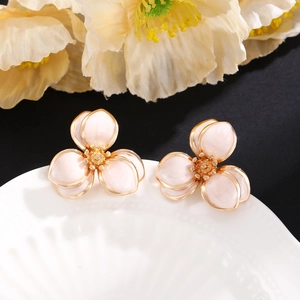 Nahaufnahme der rosa Emaille-Ohrstecker in Blumenform mit Goldrand auf weißem Teller