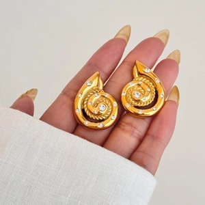 Golden spiral shell stud earrings with white zircon crystals held by a model