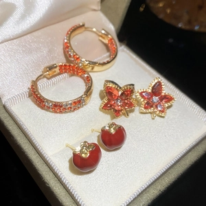 Detailed view of autumn-themed maple leaf and persimmon earrings set with zircons