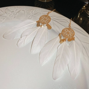 Close-up of bohemian hollow gold earrings with elegant white feather tassels on ceramic