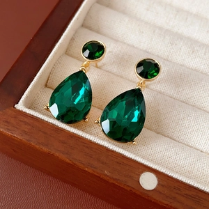 Macro shot of green teardrop earrings with gold base in a soft beige jewelry box