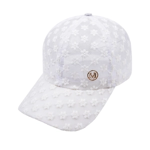 Détail de la dentelle florale blanche et du logo métallique doré M sur la casquette