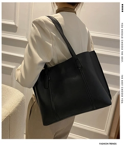 Side view of a large black matte leather tote bag worn by a model against a white wall