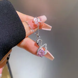 Detail of silver swan necklace featuring a large pink zircon held by manicured fingers