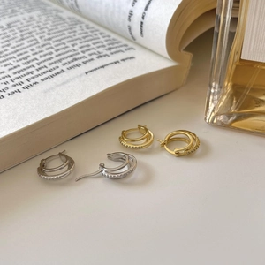 Detailed shot of double hoop earrings with cubic zirconia near a book and perfume