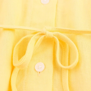 Détail de la texture du chemisier en lin jaune avec boutons blancs et nœud à la taille