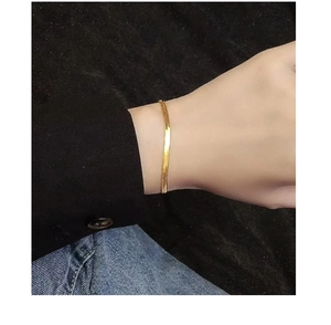 Detail of a minimalist gold flat snake bone chain bracelet worn on a female wrist