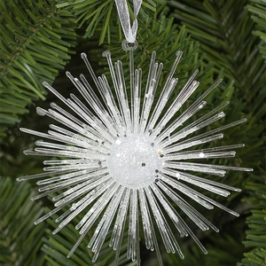 Sparkling silver starburst Christmas ornament hanging on a green pine tree branch