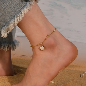 Close-up of gold shell and starfish charm anklet on model's ankle at the beach