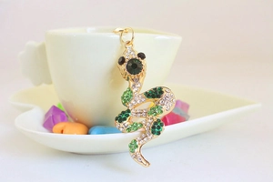 Detail of a golden snake keychain encrusted with green and white rhinestones on a dish