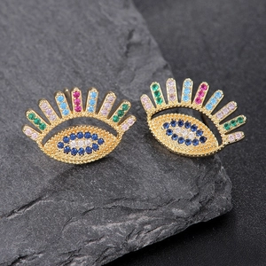 Golden evil eye safety pin earrings with colorful crystals on dark slate stone