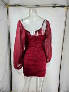 Detail view of the back of a red ruched mini dress with sheer mesh long sleeves and a zipper