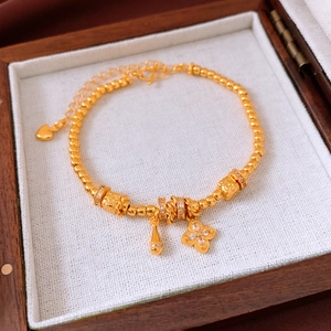 Macro shot of 24K gold plated beaded bracelet with clover charm in wooden jewelry box