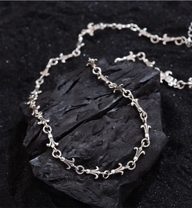 Macro shot of silver iris cross pendant on a textured black rock, vintage aesthetic