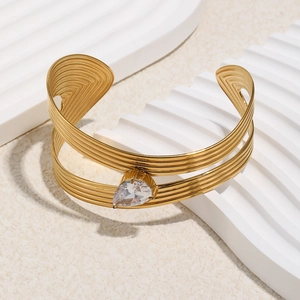 Détail d'un bracelet jonc rayé plaqué or 18 carats avec zircon goutte sur marbre blanc