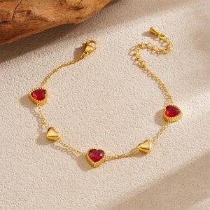Detail of gold-plated bracelet with alternating red heart gems and golden heart charms