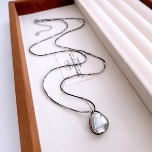 Close-up of minimalist silver teardrop pendant on a layered chain in a gift tray