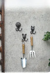 Detail of vintage cast iron animal wall hooks holding garden tools on a textured wall