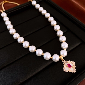Macro detail of gold-plated flower pendant with red gemstone on pearl necklace