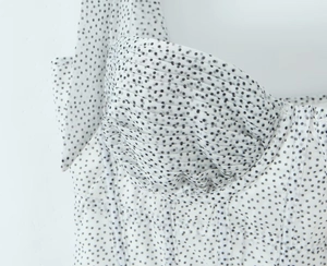 Detailed close-up of white chiffon dress with black polka dots and pleated chest design