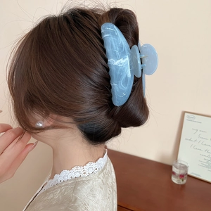 Détail d'une pince à cheveux en acrylique bleu marbré tenant des cheveux épais