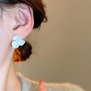 Detailed close-up of a white flower earring with a lustrous pearl on a female model