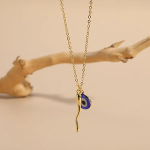 Detail of 14K gold plated necklace featuring glass evil eye and chili charms on beige decor