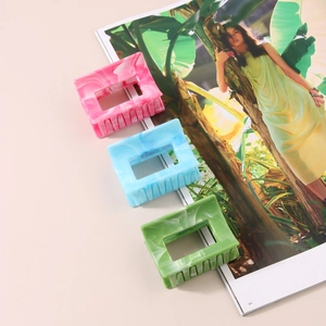 Three rectangular marble pattern hair claws in pink, blue, and green on a magazine