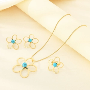 Détail d'une parure en or avec fleurs ajourées et perles turquoise bleues sur tissu beige