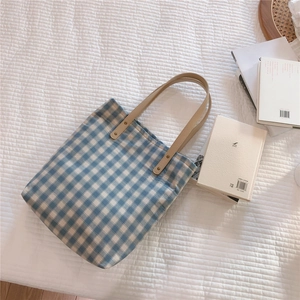 Close-up of blue plaid canvas tote with leather handle and metal rivet details