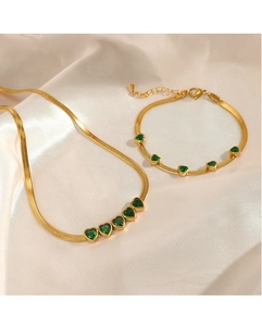 Close-up of golden snake chain jewelry set with emerald heart gemstones on silk