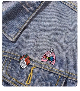 Detail of anatomical heart and lung enamel pins attached to a blue denim jacket pocket