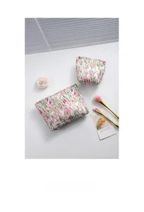 Detail shot of floral fabric makeup bags with two brushes and a rose on white surface